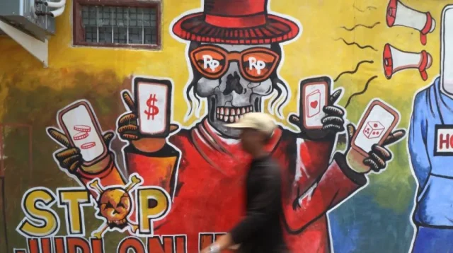 Warga melintas di depan mural bertema cegah judi online di Kediri, Jawa Timur, Rabu (9/10/2024). Mural karya Kapolsek Plemahan AKP Bowo Wicaksono yang memiliki hobi melukis tersebut sebagai upaya edukasi sekaligus mendukung pemerintah mencegah judi online kepada masyarakat. ANTARA FOTO/Prasetia Fauzani/foc.